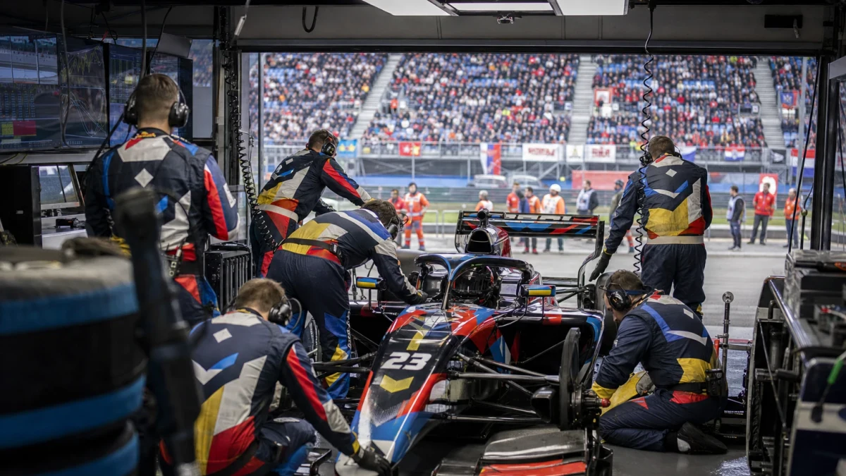 Mekaniker i lagoveraller arbetar runt en formelbil i depagaraget.