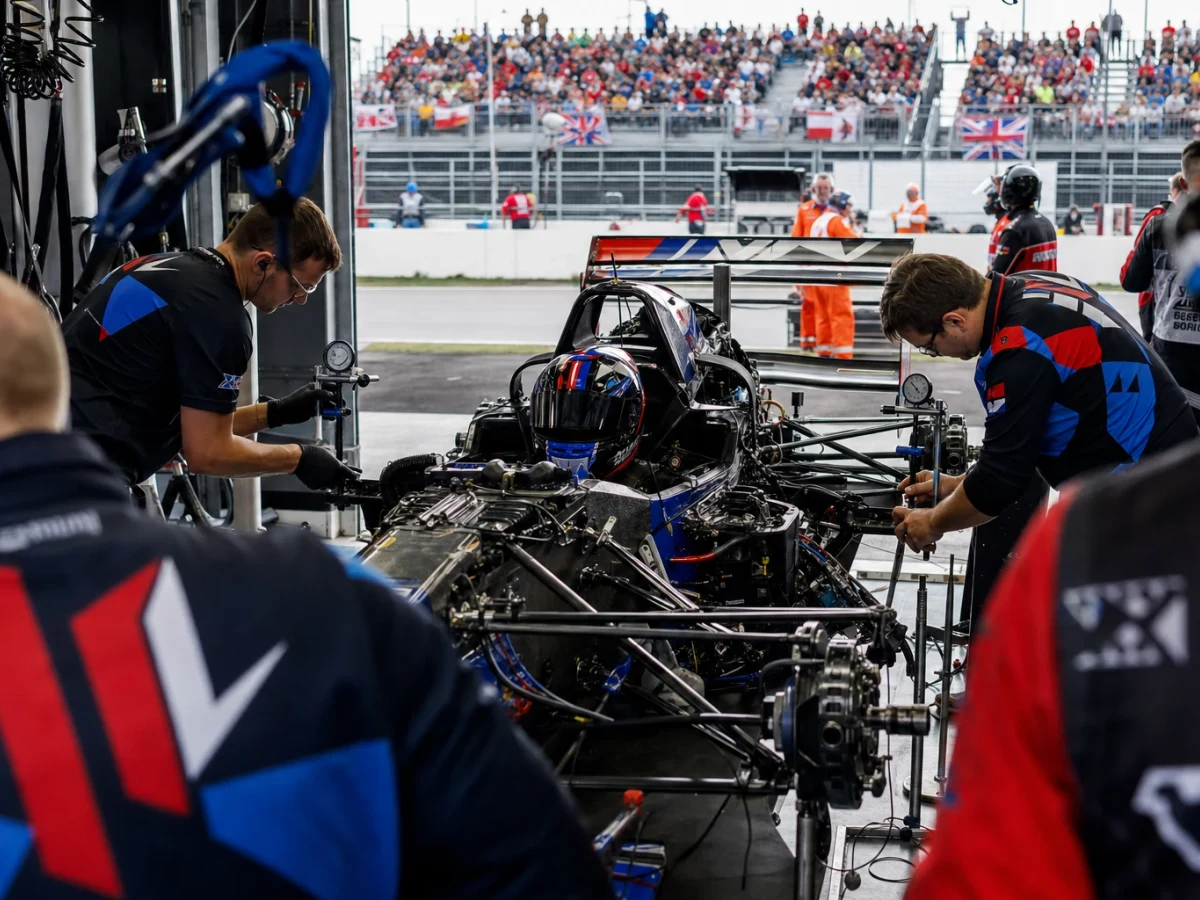 Grön formel 1-bil i depån medan mekaniker samlas runt bakvagnen.
