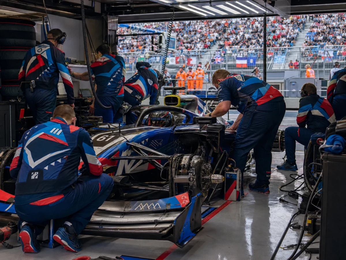 Formel 1-bil i blått och vitt genom en snabb kurva i skarpt kvällsljus, sedd bakifrån.